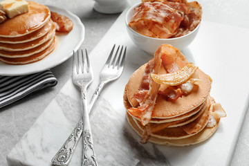 Marble board with pancakes, bacon and fried banana on table