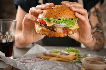 Woman holding tasty beef burger over table