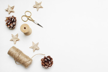 Christmas festive styled stock image composition. Pinecones, golden scissors, rope and wooden stars on white wooden background. Gift wrapping. Flat lay, top view.