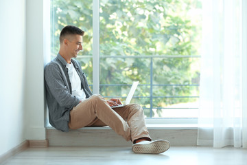 Young man using laptop near window at home