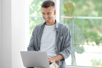 Young man using laptop near window at home