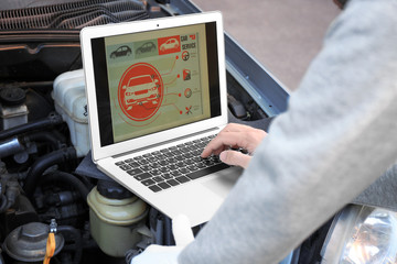 Young male mechanic using computer diagnostic while repairing car