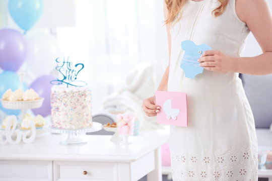 Pregnant woman holding cards for baby shower party, indoors