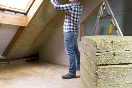 Man installing thermal roof insulation layer  - using mineral wool panels. Attic renovation and insulation concept