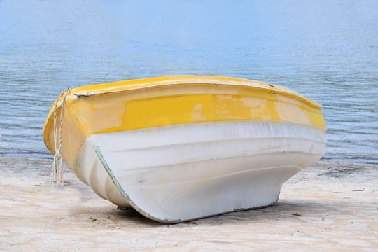 Kleines verlassenes Holzboot liegt am Strand, das Meer mit seichten Wellen im Hintergrund