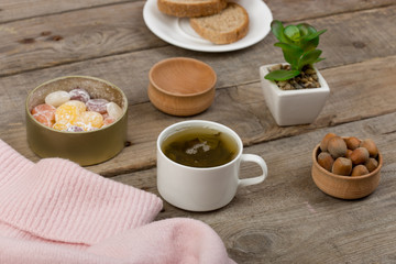 Winter cozy concept - the cup of tea, candy, nuts and pink sweater on brown wooden table