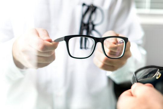 Optician showing new glasses to customer for trying. Eye doctor giving patient lenses.
