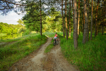Naklejka premium The girl rides a bike on the forest road.