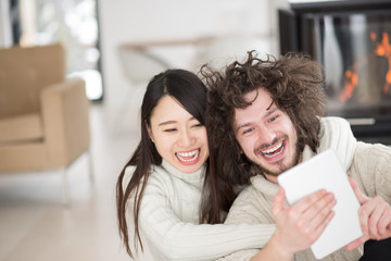 multiethnic couple using tablet computer in front of fireplace