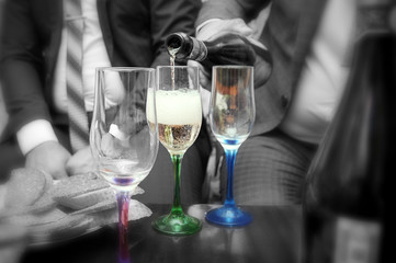 pour champagne from the bottle in the colored glasses, at the wedding, black and white background