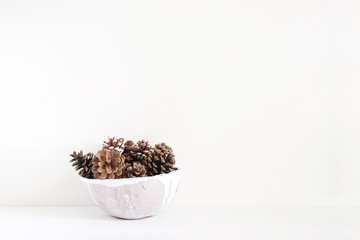 Pinecones in ceramic bowl on white table. Christmas styled stock photo, holiday background.