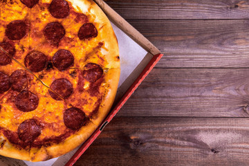 Pizza with salami in a box on a wooden background with copy space. Top view.