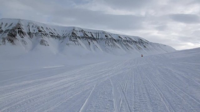 People expedition on snowmobile in North Pole Spitsbergen Svalbard Arctic. Way from airport Longyear to Pyramiden on background of glacier.