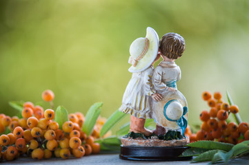 A figurine of a boy and a girl on a natural green background, rowan berries.
