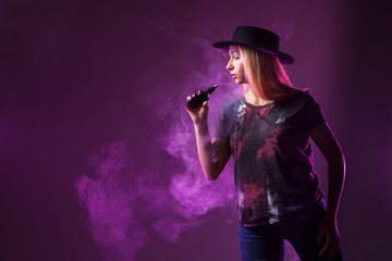Fototapeta premium Girl Vape. The girl exhales smoke from an electronic cigarette. The girl is a Vaper in the hat.