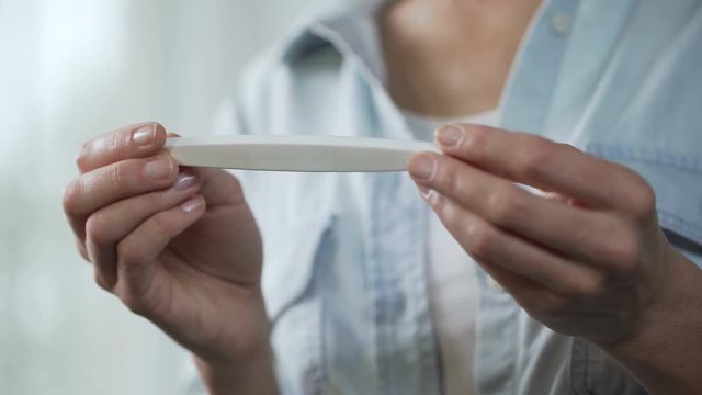 Female holding negative pregnancy test in hands, demonstrating before camera