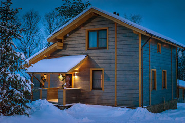 Winter evening. Snow-covered cottage. Wooden two-storey house. Cottage in winter.