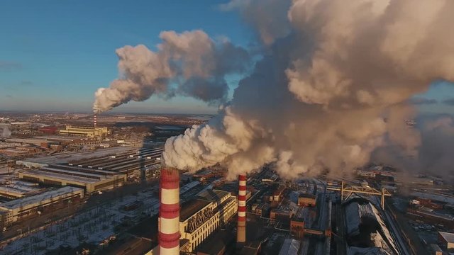 Pipes with smoke: industrial production, plant, air pollution. Dense thick smoke comes from industrial red-white pipes: from a bird's eye view. Industrial zone: smoke comes from the pipe.