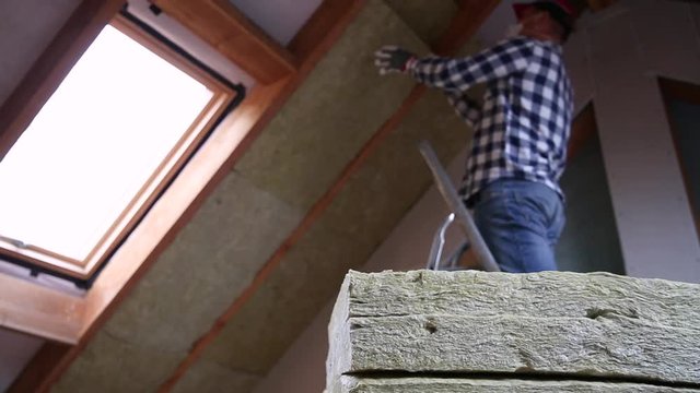 Man installing thermal roof insulation layer  - using mineral wool panels. Attic renovation and insulation concept
