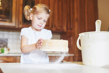 A happy girl wears a dough. Baby make dinner in chef suit