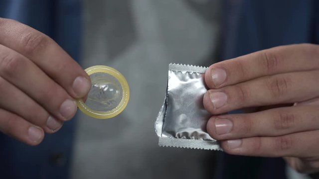 Man getting condom out of package and showing it into camera, sex and healthcare