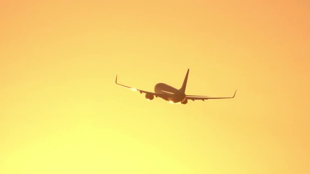 CLOSE UP: Passenger airplane flying at golden sunset. Airliner jet flying against the sunny golden sky at sunrise. People flying home from summer vacation travel by plane. Cargo plane shipping goods