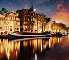 Beautiful night in Amsterdam. Night illumination of buildings and boats near the water in the canal. - obrazy, fototapety, plakaty