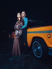 Young couple near yellow taxi car in night time