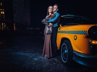 Young couple near yellow taxi car in night time