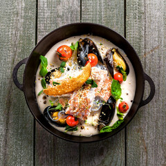 Sea bass fish fillet with mussels, crab meat and cockles with vegetables, cream sauce and rice noodles. Healthy Asian seafood meal on a table. Top view.