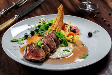 Delicious medium rare meat steak with sauce and salad on a plate. Healthy food made of meat fillet and fresh herbs on a wooden table.