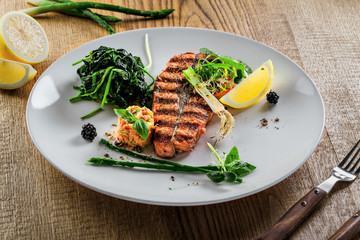 Grilled salmon fish steak with vegetable salad on a plate. Gourmet seafood meal made of fish and vegetables. Healthy food on a table.