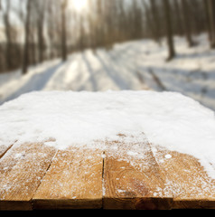 Wooden desk covered by snow and snowy park on background