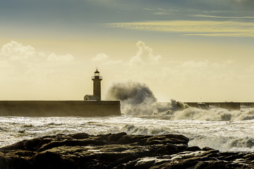 Landscape seascape lighthouse battered by huge waves on Atlantic Ocean with blue green skies and...