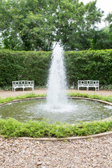 outdoor garden fountain with white bench and lush plant wall in park.