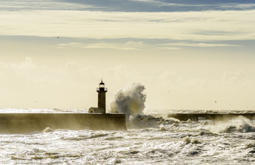 Landscape seascape lighthouse battered by huge waves on Atlantic Ocean with blue green skies and...