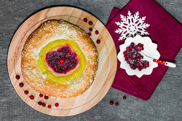 Cake of yeast dough with lemon cream and berries cranberries on a wooden plate with a linen napkin and a snowflake on a wooden table vintage top view
