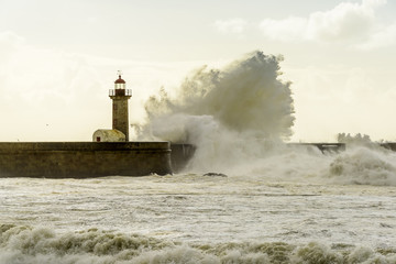Landscape seascape lighthouse battered by huge waves on Atlantic Ocean with blue green skies and...