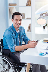 Be positive. Happy man keeping smile on his face and holding telephone while sitting in semi position