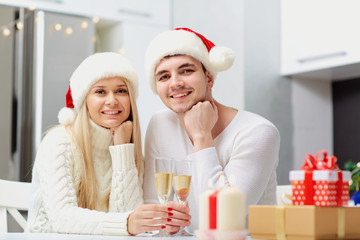 A couple in Santa Claus hats with champagne glasses on Christmas. Husband and wife in the New Year in the room.