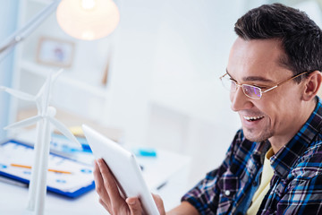 Busy man. Handsome man expressing positivity and bowing head while examining tablet