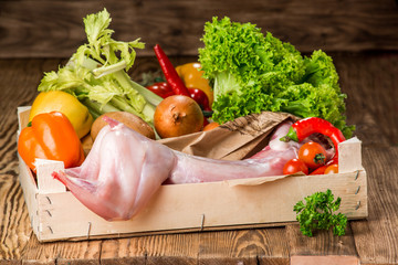 Raw whole rabbit with vegetables and spices on a dark rustic background.