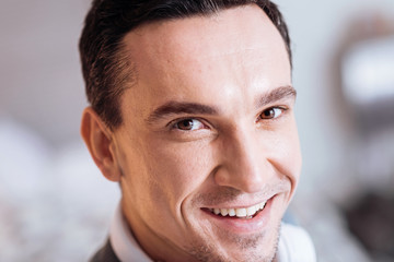 Obraz premium Sincere person. Positive brunette keeping smile on his face and looking forward while being at home