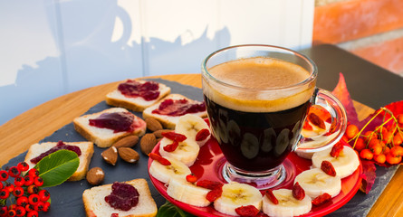 A cup of coffee, bread with confiture, almonds, banana, berries on the outside give a shadow in the rays of the dawn.