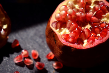 Cut red juicy pomegranate on a black background with shadows.