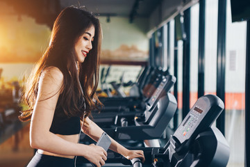 Fototapeta na wymiar Asian woman exercising in the gym, Young woman workout in fitness for her healthy and office girl lifestyle. She listening the music while exercising.