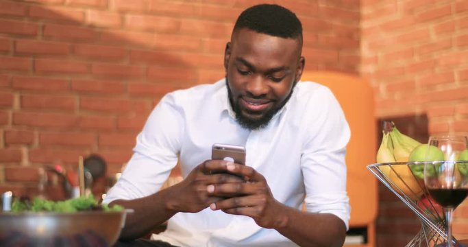 Portrait young black man use phone smiling in kitchen home communication curly face guy internet mobile model nigerian technology touch cell cool african afro american Slow Motion Shot