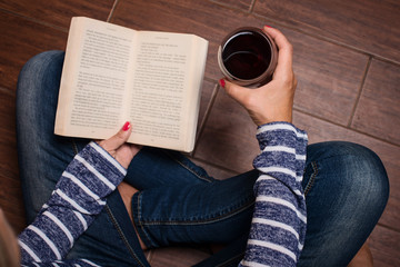 Fototapeta premium Leisure, drinks, education and lifestyle concept. Woman sitting on the floor, holdind book and glass of red wine. Woman having a glass of wine and reading.