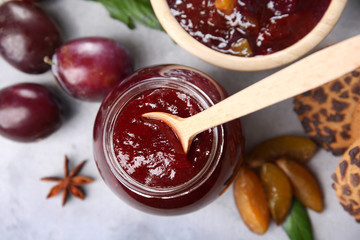 Glass jar with delicious plum jam on table