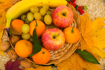 Fruits are in the basket. grapes; apples; clementines; nuts; banana; yellow leaves;